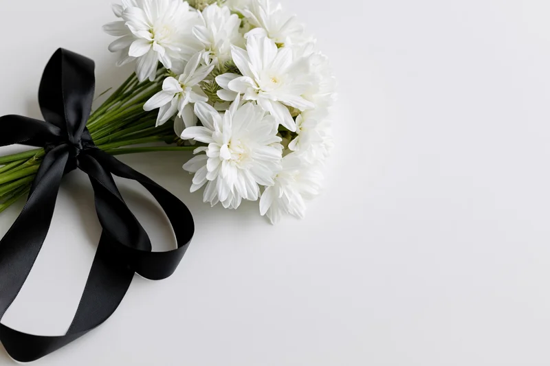 Small bouquet of white chrysanthemums tied with black satin ribbon on white surface