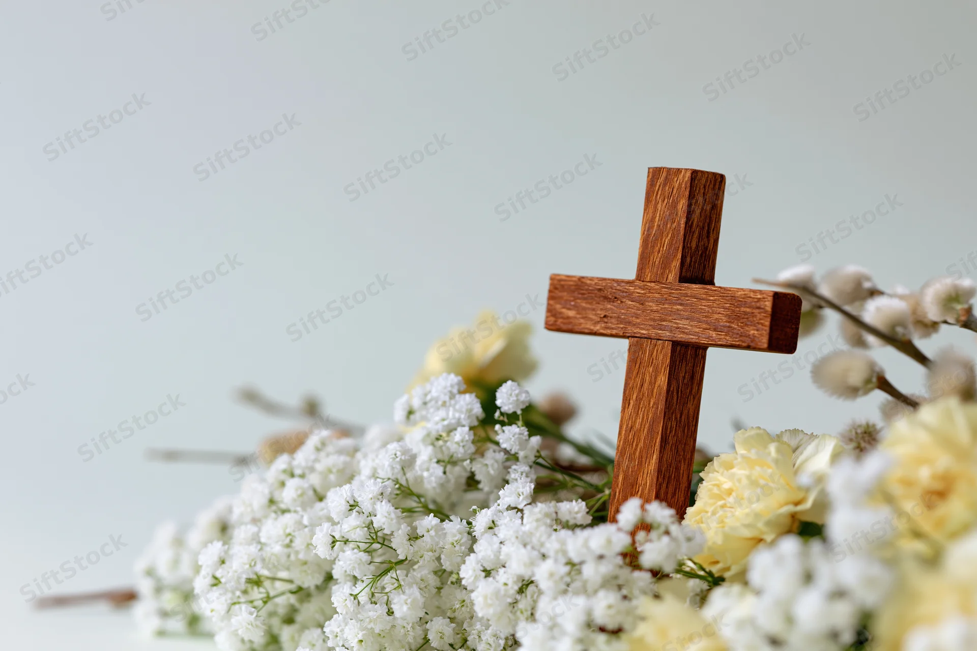 Wooden cross standing among white and yellow flowers on a light background