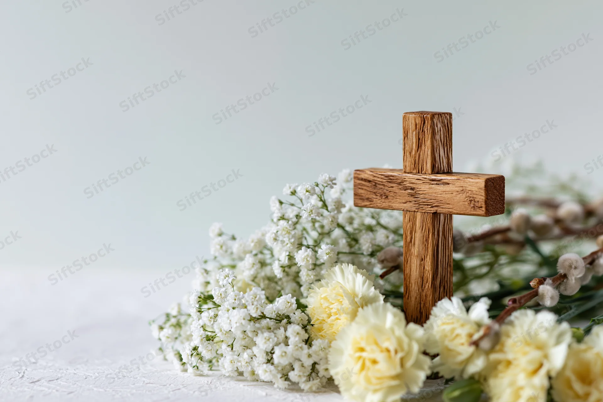 Wooden cross standing among white flowers and baby's breath on a light surface