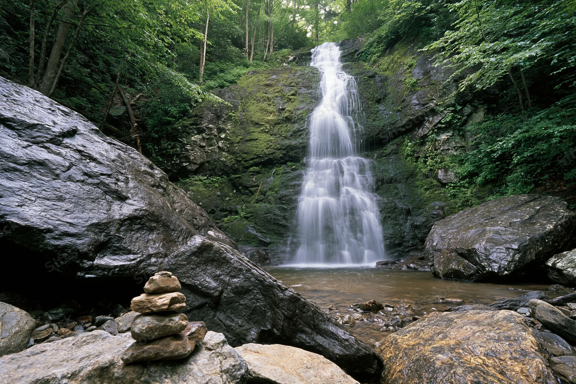 Multi-tiered waterfall cascading down moss-covered rocks in a dense forest