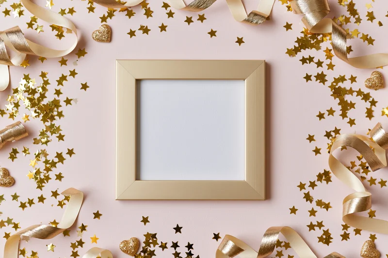 Gold picture frame with blank white interior surrounded by gold confetti and ribbons on pink background