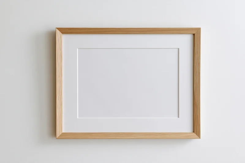 Light oak wooden picture frame with white mat board hanging on a plain white wall