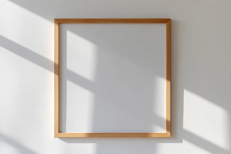 Light wood picture frame with blank white interior mounted on a white wall with sunlight casting shadows