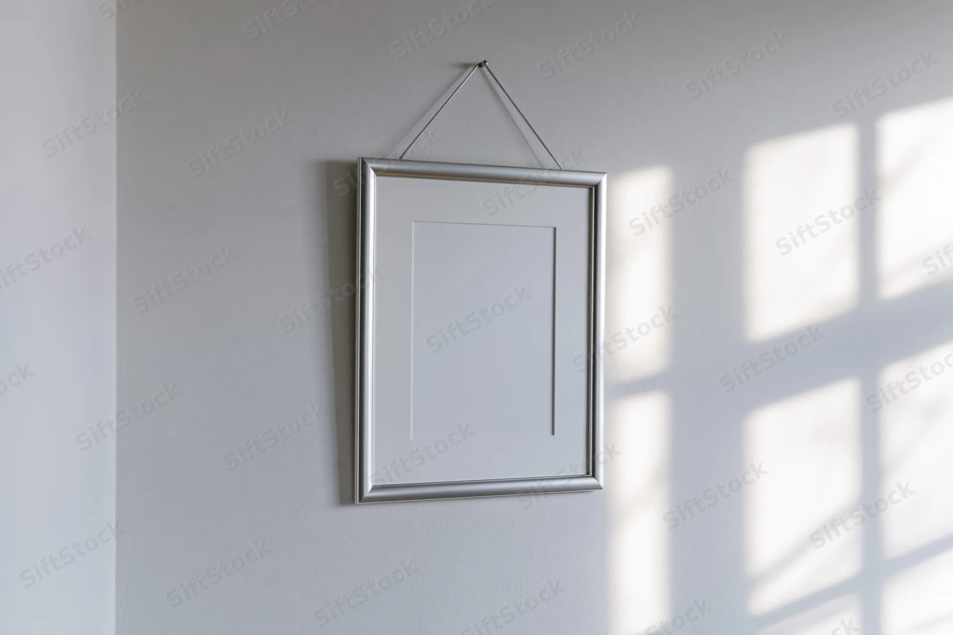 Silver metal picture frame hanging on a white wall with sunlight casting window shadows