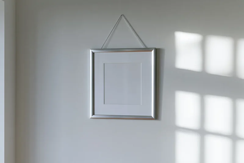 Silver metal picture frame hanging on a plain white wall with window shadow pattern