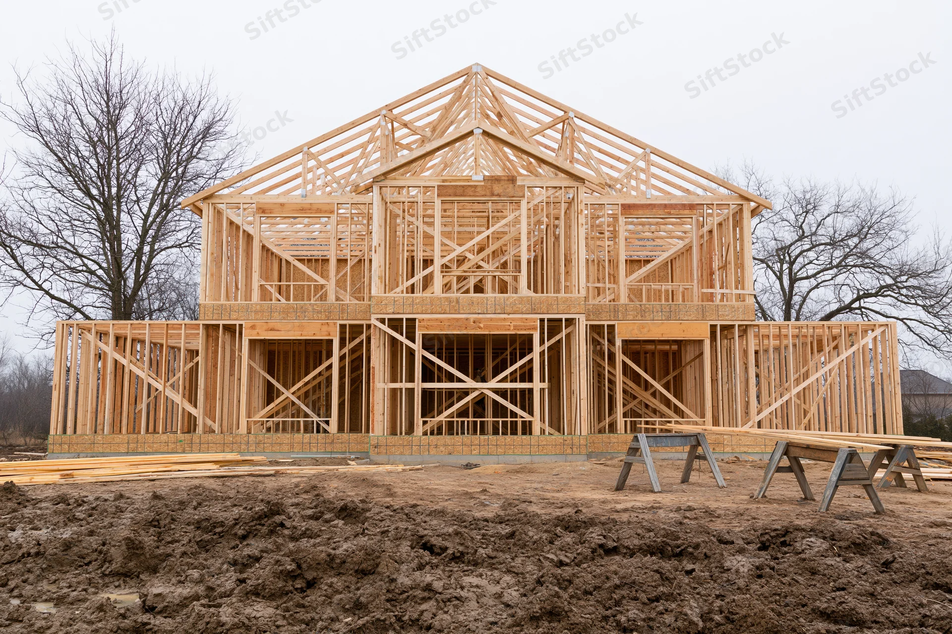 Two-story residential house under construction with wooden frame exposed on muddy site