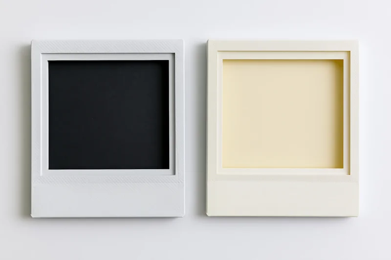 Two blank polaroid film frames side by side on white surface