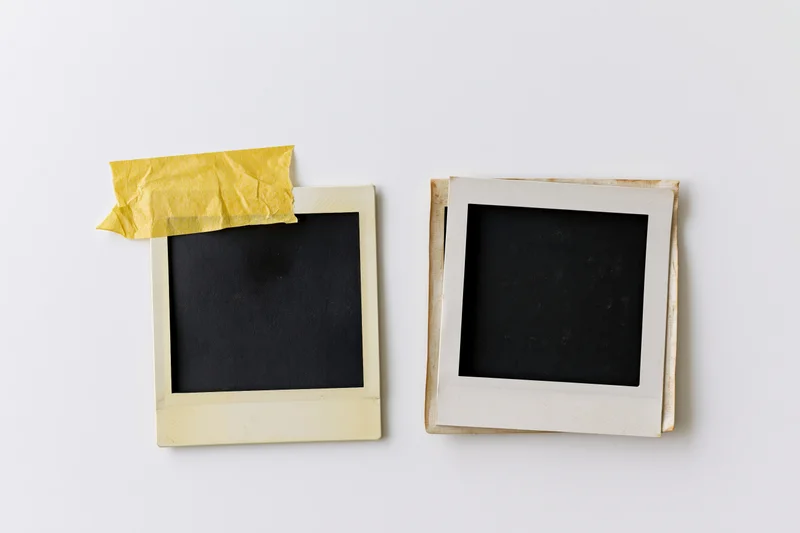 Two blank vintage polaroid photo frames lying flat on white surface with yellow tape and copyspace