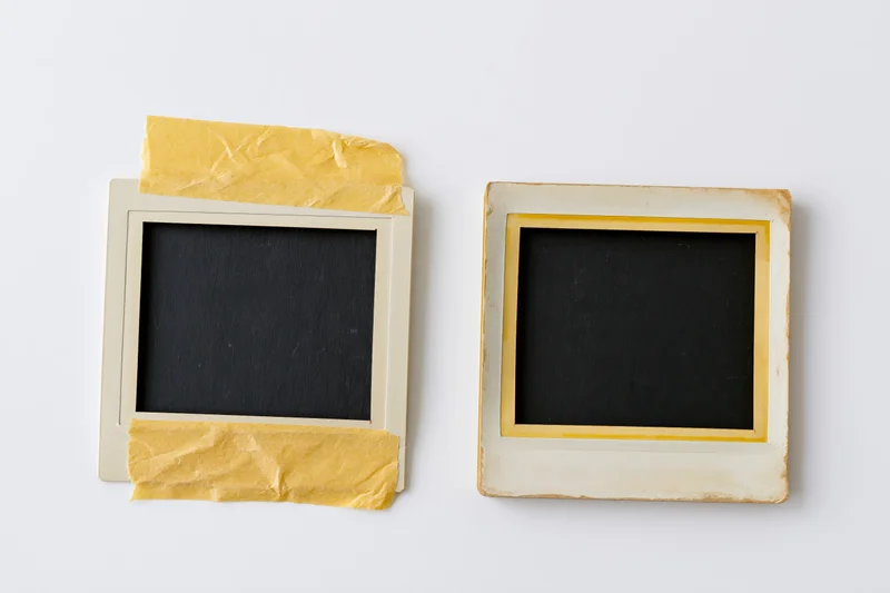 Two vintage polaroid photo frames lying flat on white surface with yellow tape and blank black centers