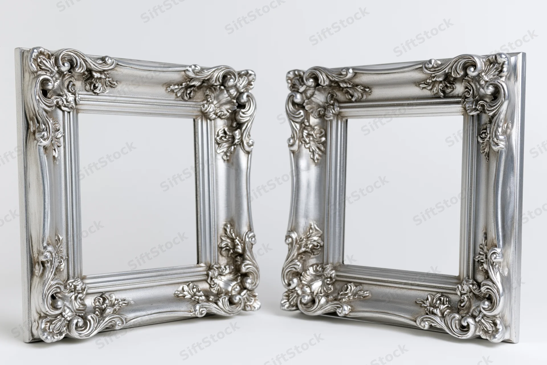 Two ornate silver picture frames with baroque and rococo carvings standing side by side on a white surface
