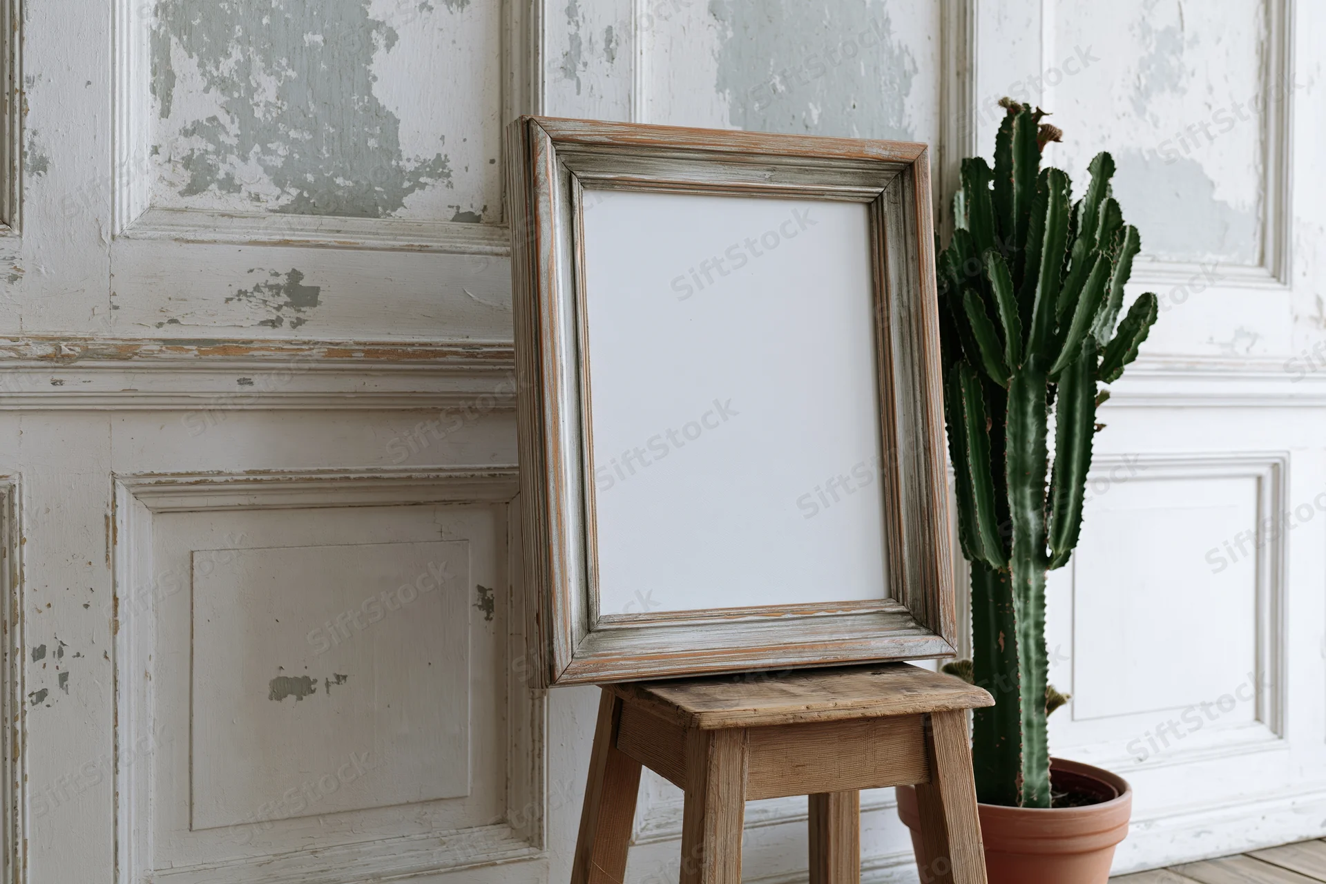 Weathered wooden frame leaning on a stool beside a potted cactus against peeling white paneling