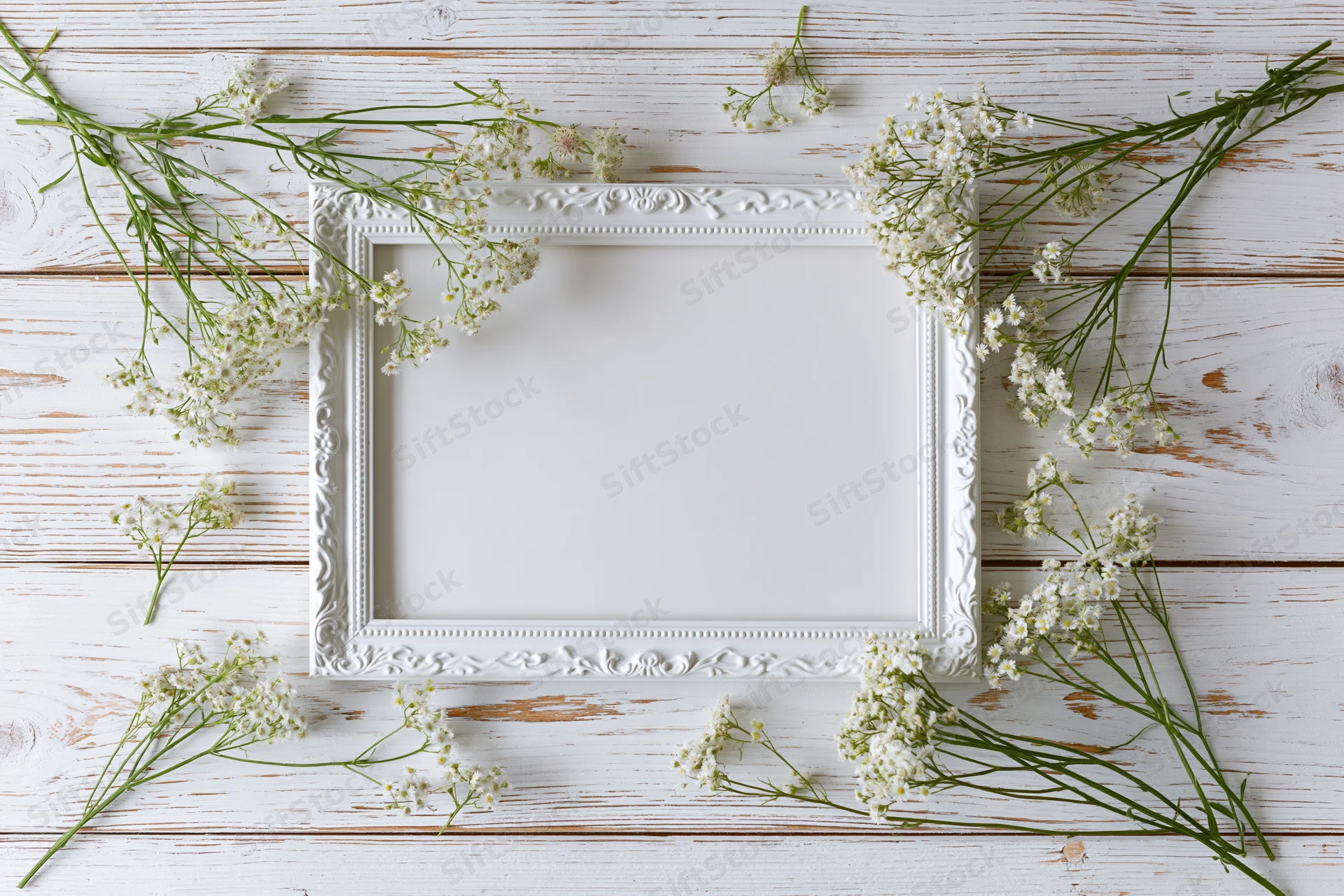 White ornate frame with baby's-breath flowers arranged around it on a rustic wooden surface