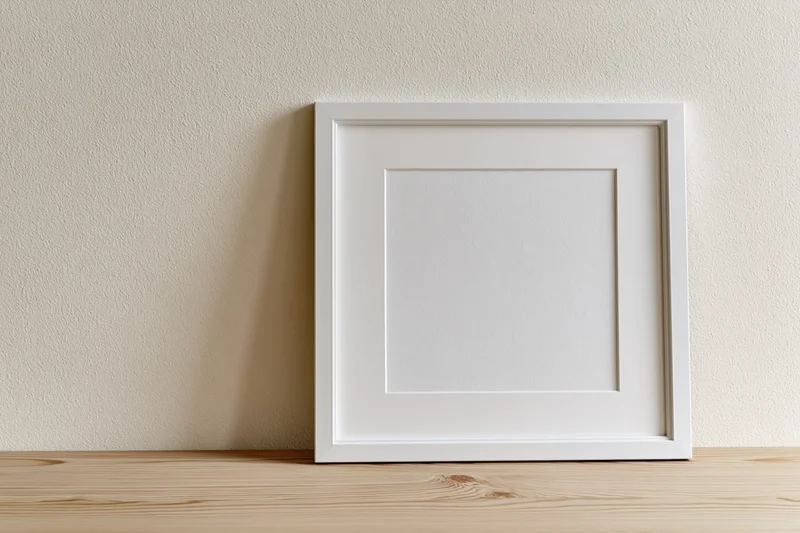 White picture frame with wide mat leaning against textured wall on wooden shelf