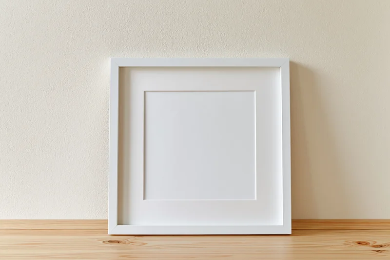 White picture frame with wide mat leaning against textured wall on wooden shelf