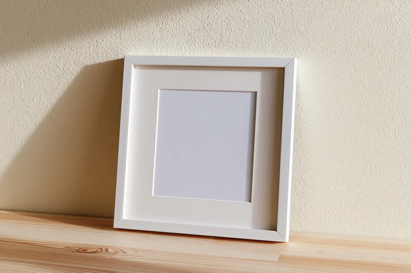 White picture frame with wide mat leaning against textured wall on wooden shelf