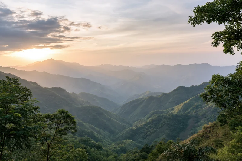 Layered green mountain ridges receding into misty horizon at sunset
