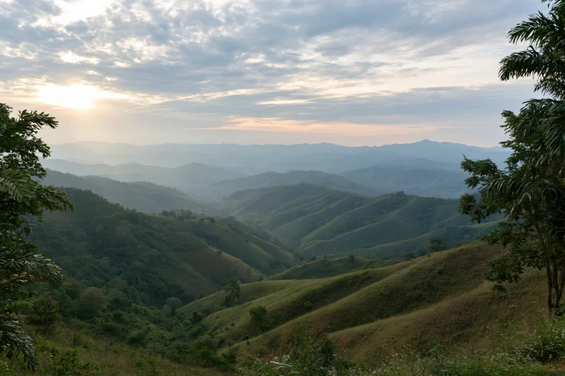 Layered green mountain ridges receding into misty horizon under cloudy sky at sunrise