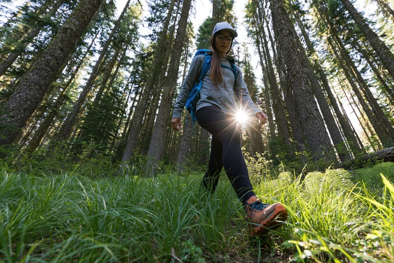 Woman hiking through dense forest with backpack stepping over grassy ground