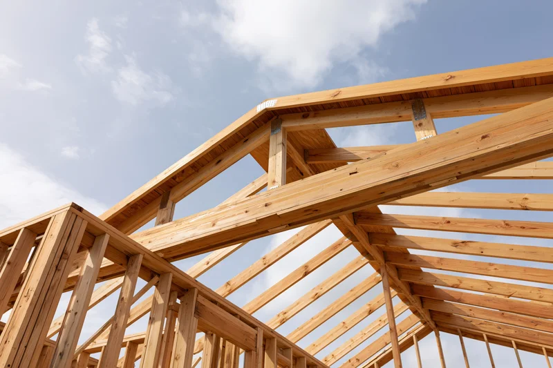 Wooden roof framing structure under construction against a blue sky