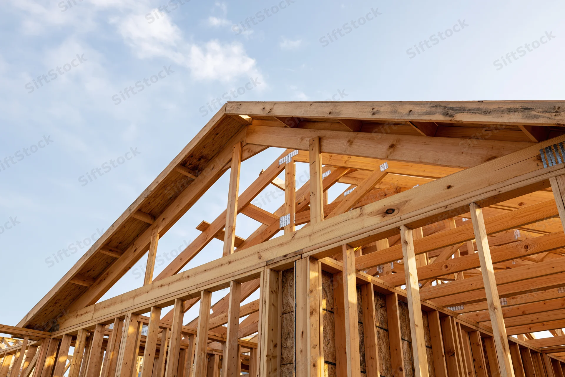 Wooden house frame under construction with exposed lumber framing against a blue sky