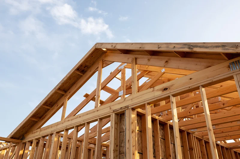 Wooden house frame under construction with exposed lumber framing against a blue sky