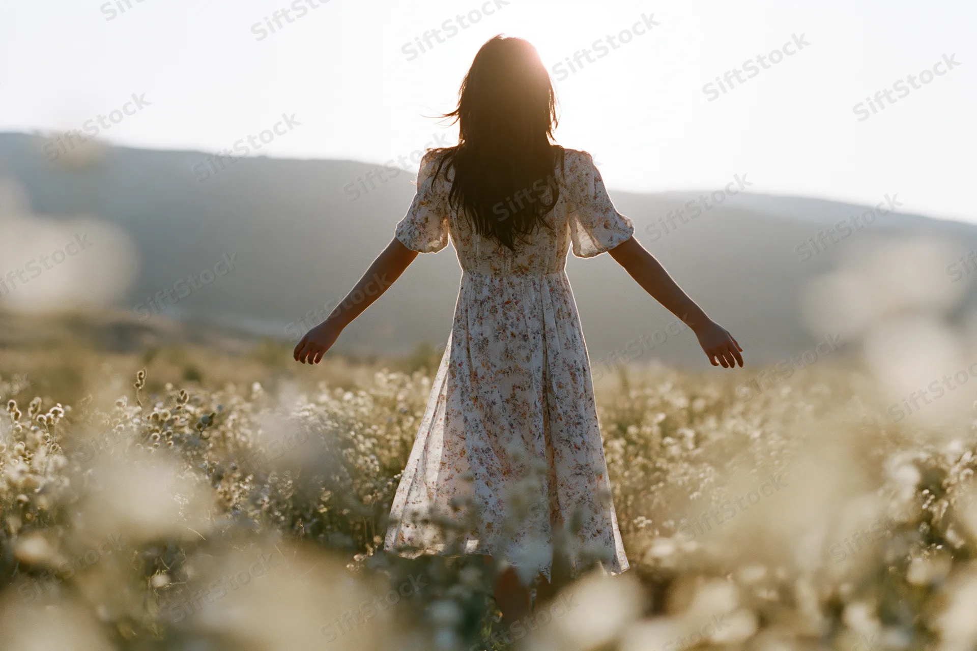 Woman with arms outstretched standing in a field of wildflowers at golden hour
