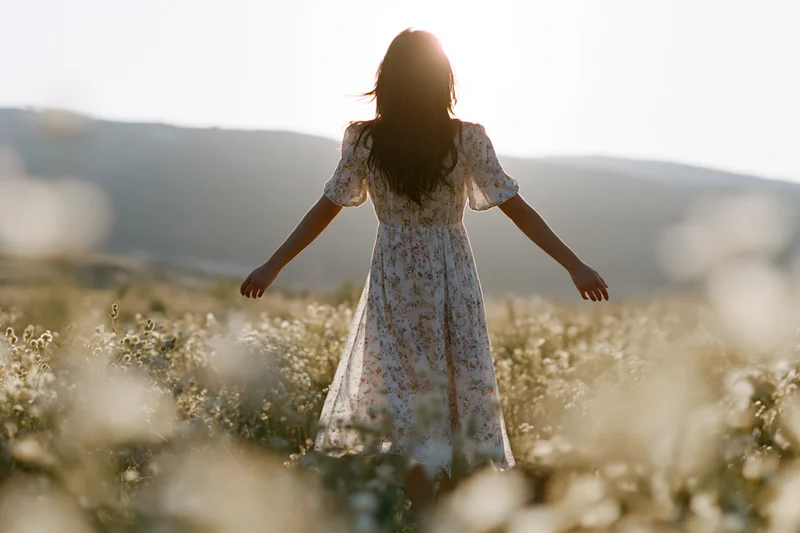 Woman with arms outstretched standing in a field of wildflowers at golden hour