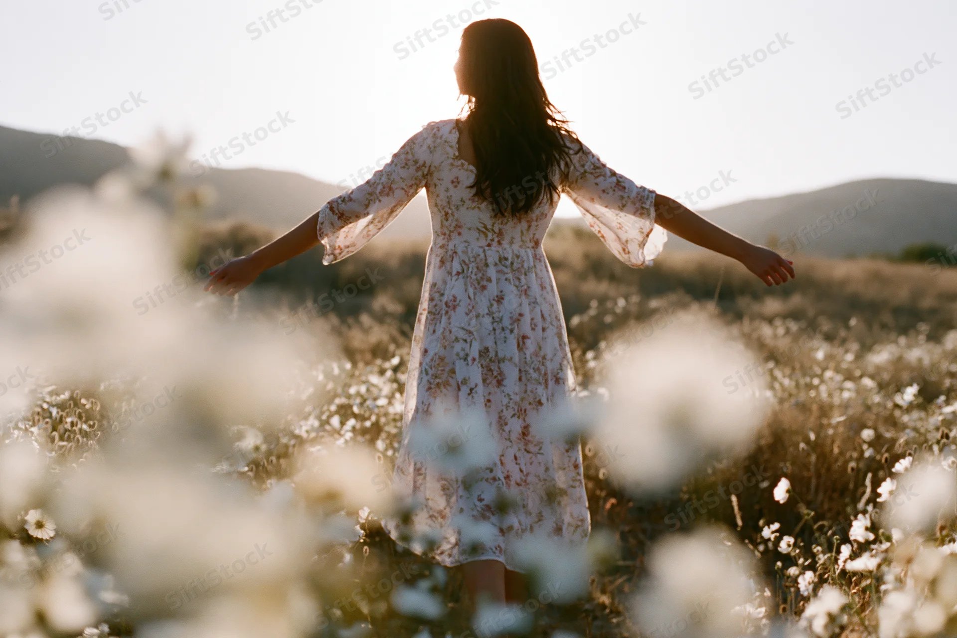 Woman with arms outstretched standing in a field of wildflowers at golden hour