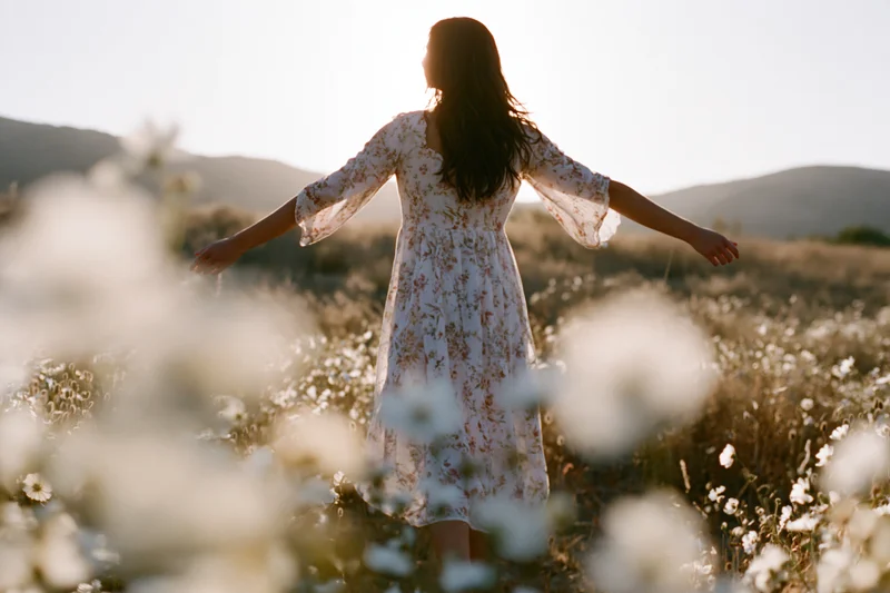 Woman with arms outstretched standing in a field of wildflowers at golden hour