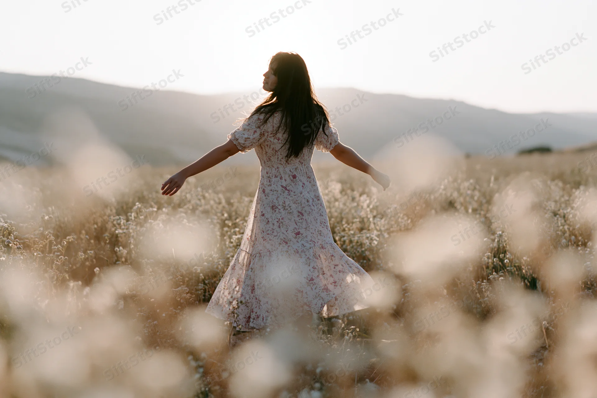 Woman standing with arms outstretched in a field of wildflowers at sunset