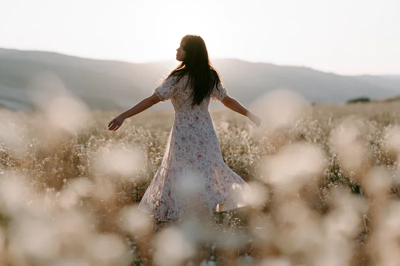 Woman standing with arms outstretched in a field of wildflowers at sunset
