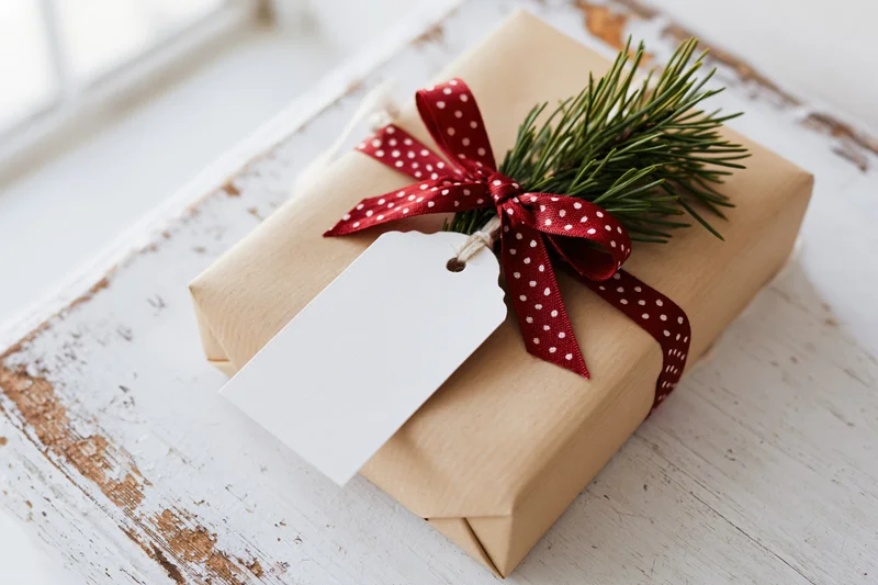 Christmas gift wrapped in brown paper with red polka dot ribbon and pine sprig on wooden surface