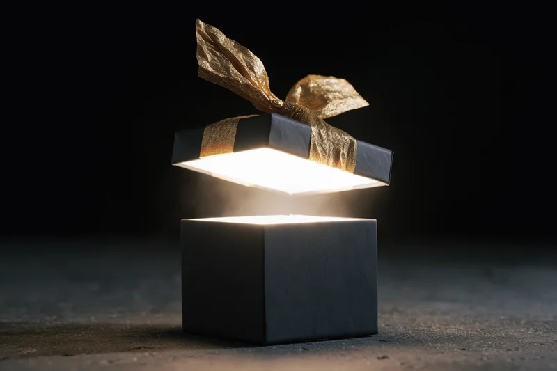 Black gift box with floating lid emitting bright light on dark surface