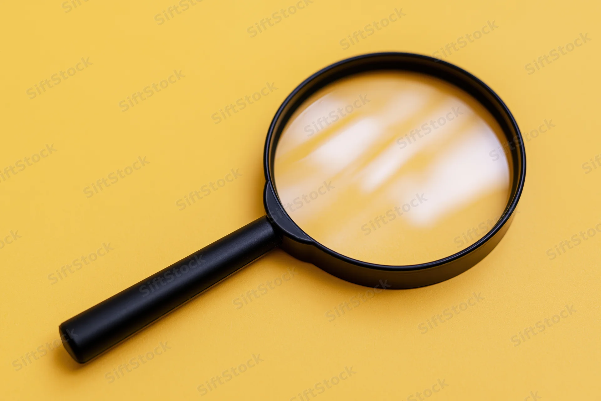 Black plastic magnifying glass lying flat on bright yellow background