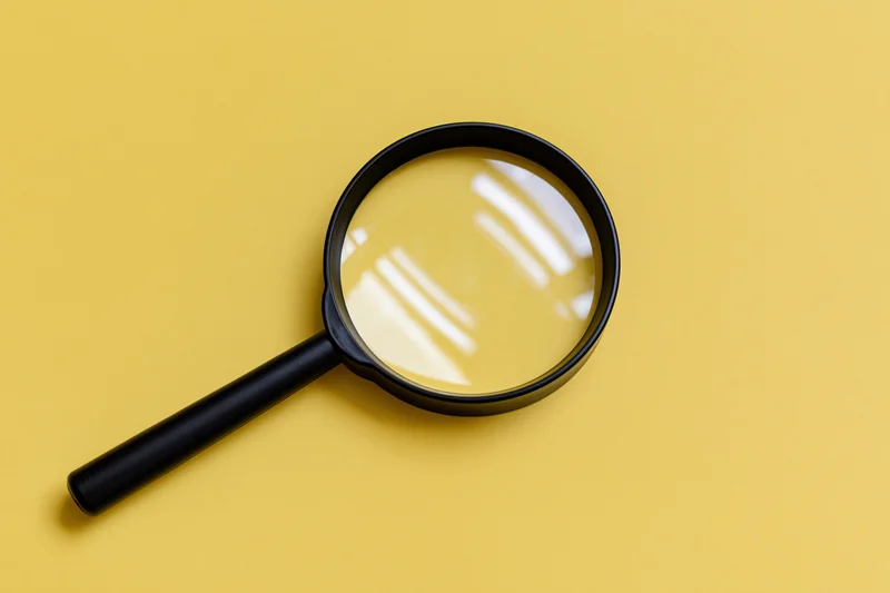 Black plastic magnifying glass lying flat on a solid bright yellow background