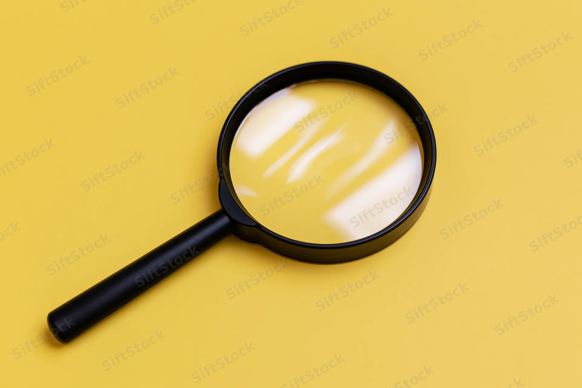 Black plastic magnifying glass lying flat on bright yellow surface