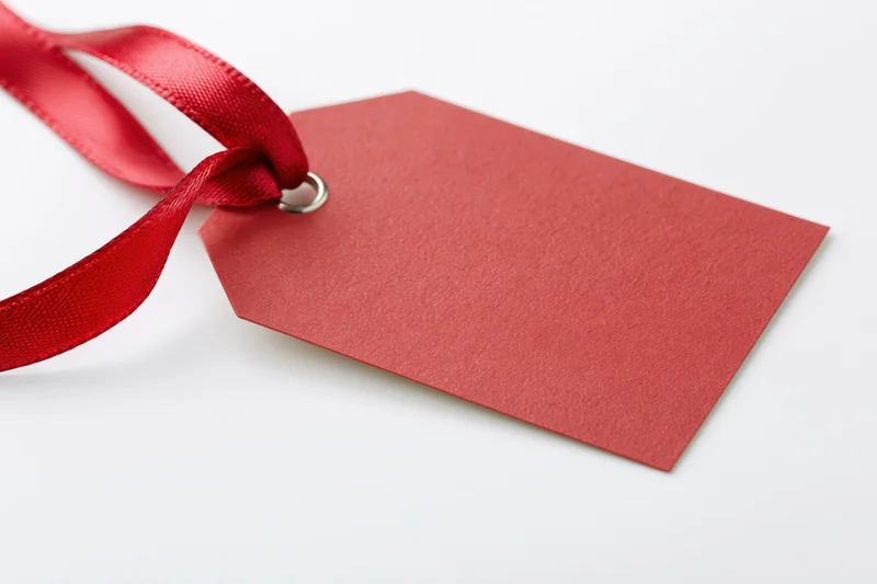Blank red paper gift tag with satin ribbon on white background