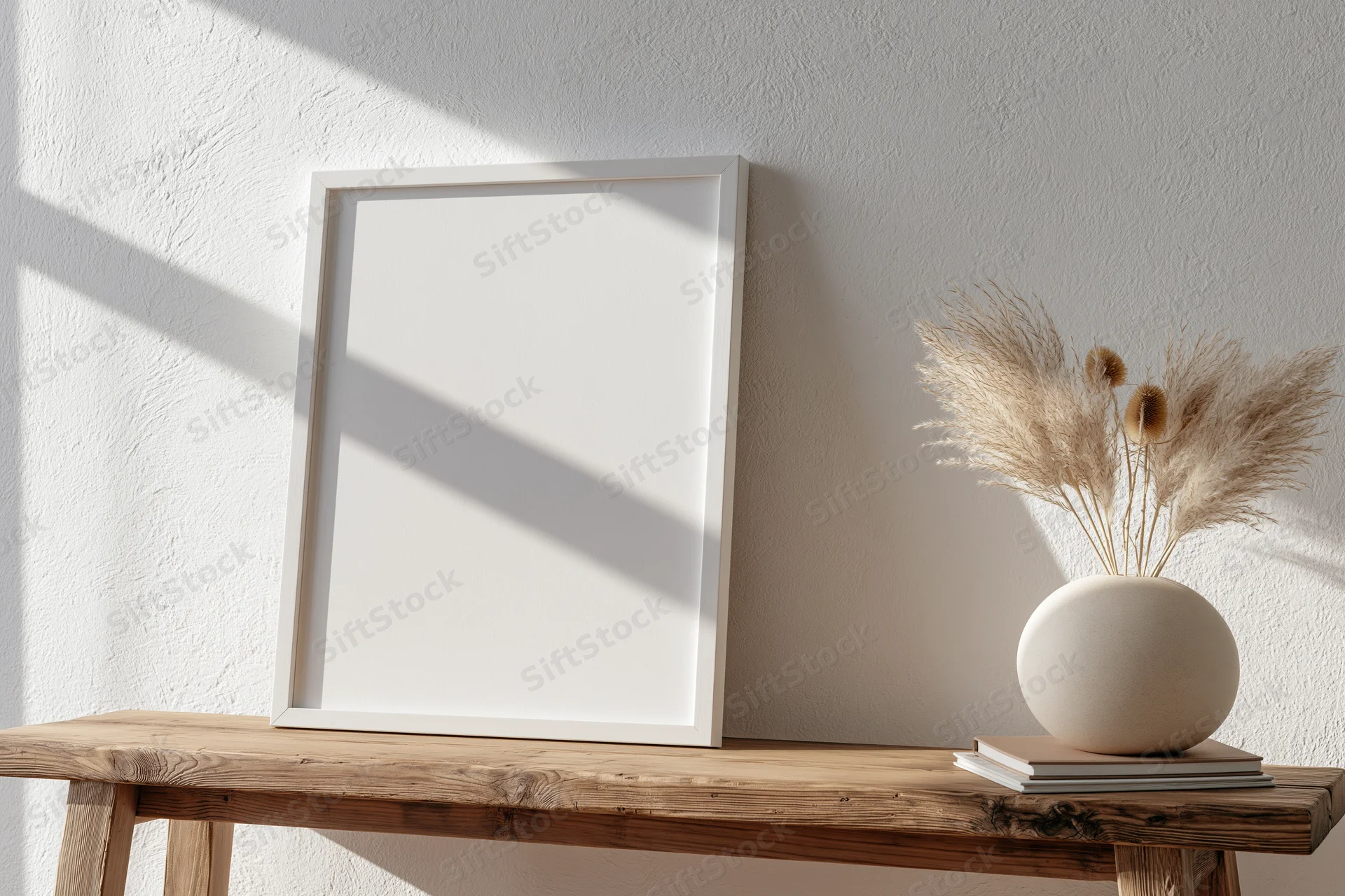 Blank white frame leaning on wooden table beside vase with dried pampas grass in minimalist interior