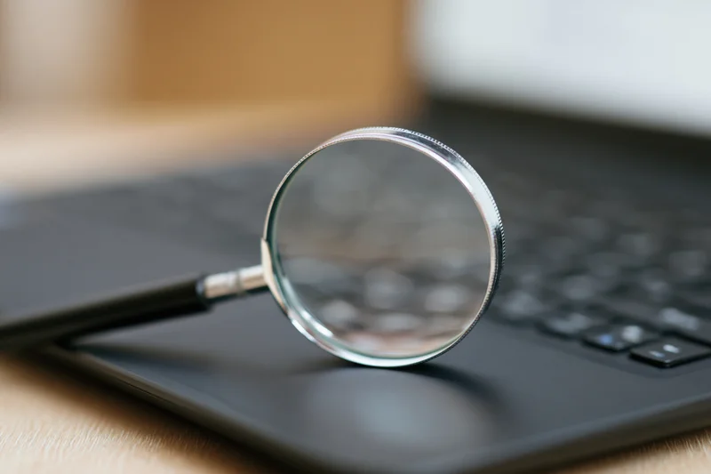 Chrome magnifying glass standing upright on black laptop keyboard on wooden desk
