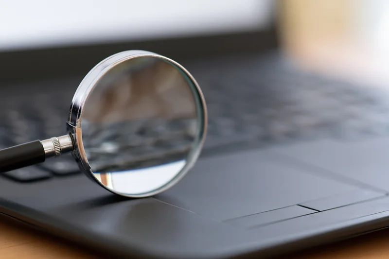 Chrome magnifying glass resting on black laptop keyboard in office workspace