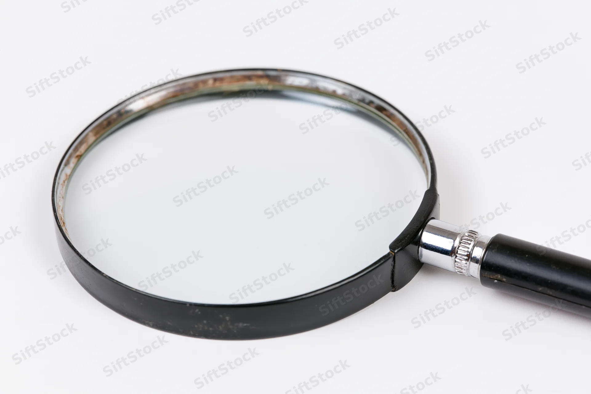 Vintage magnifying glass with black handle and metal rim lying flat on white surface