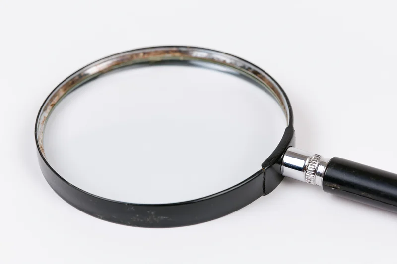 Vintage magnifying glass with black handle and metal rim lying flat on white surface
