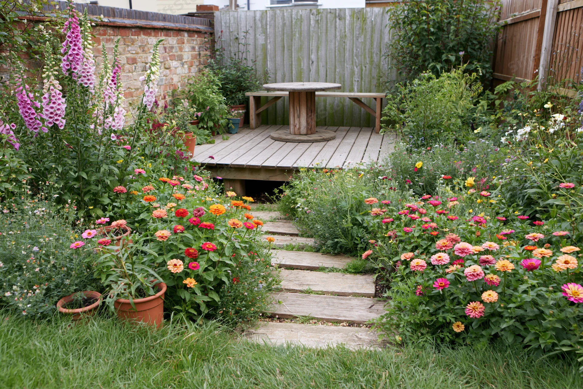 Cottage garden with colorful flowers and stone path leading to wooden deck with table and bench