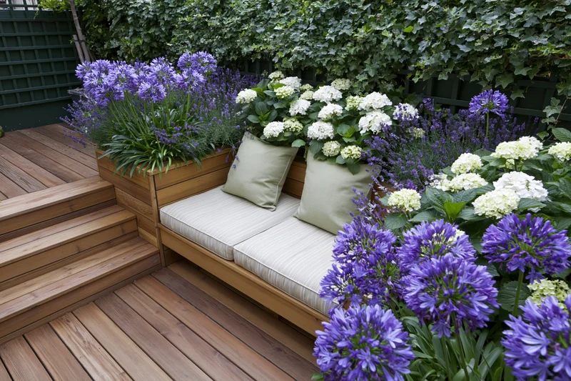 Wooden bench with cushions and flowering plants on a garden terrace