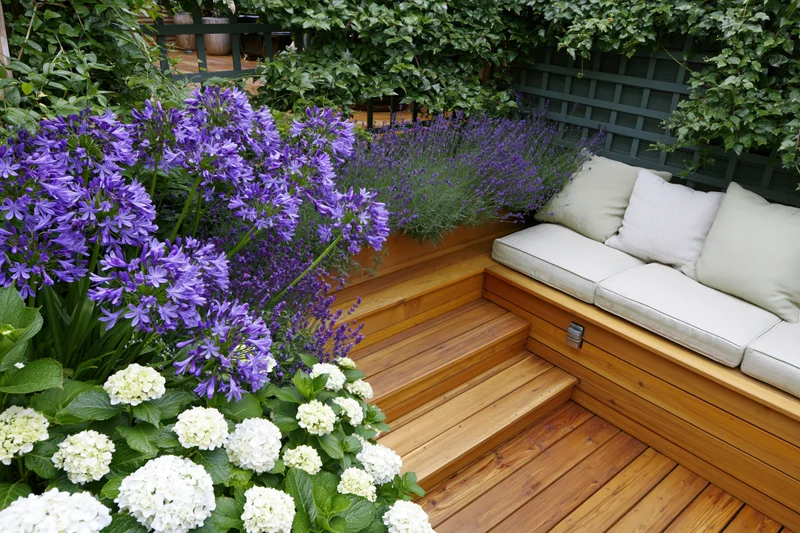 Built-in hardwood bench with cushions beside blooming purple and white flowers on a garden terrace