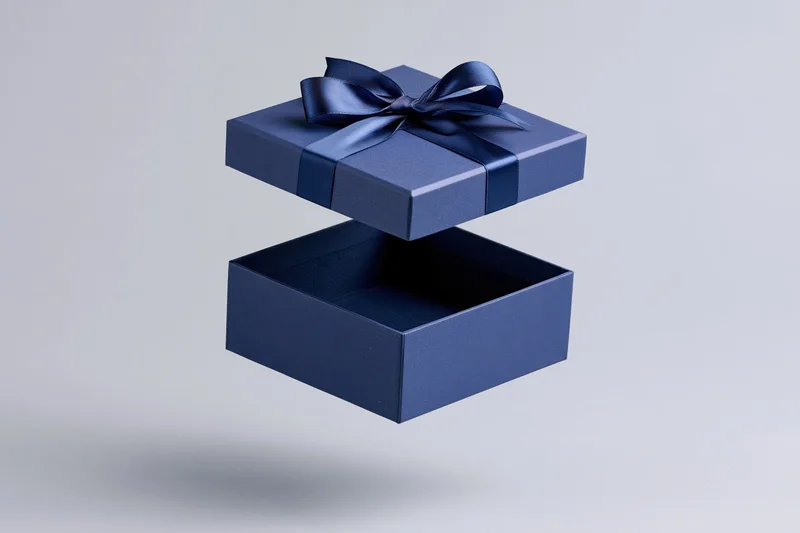 Deep blue gift box with lid floating above open base, tied with satin ribbon, isolated on light gray background