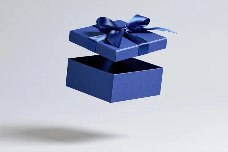 Deep blue gift box with lid floating above open base, tied with satin ribbon, isolated on white background