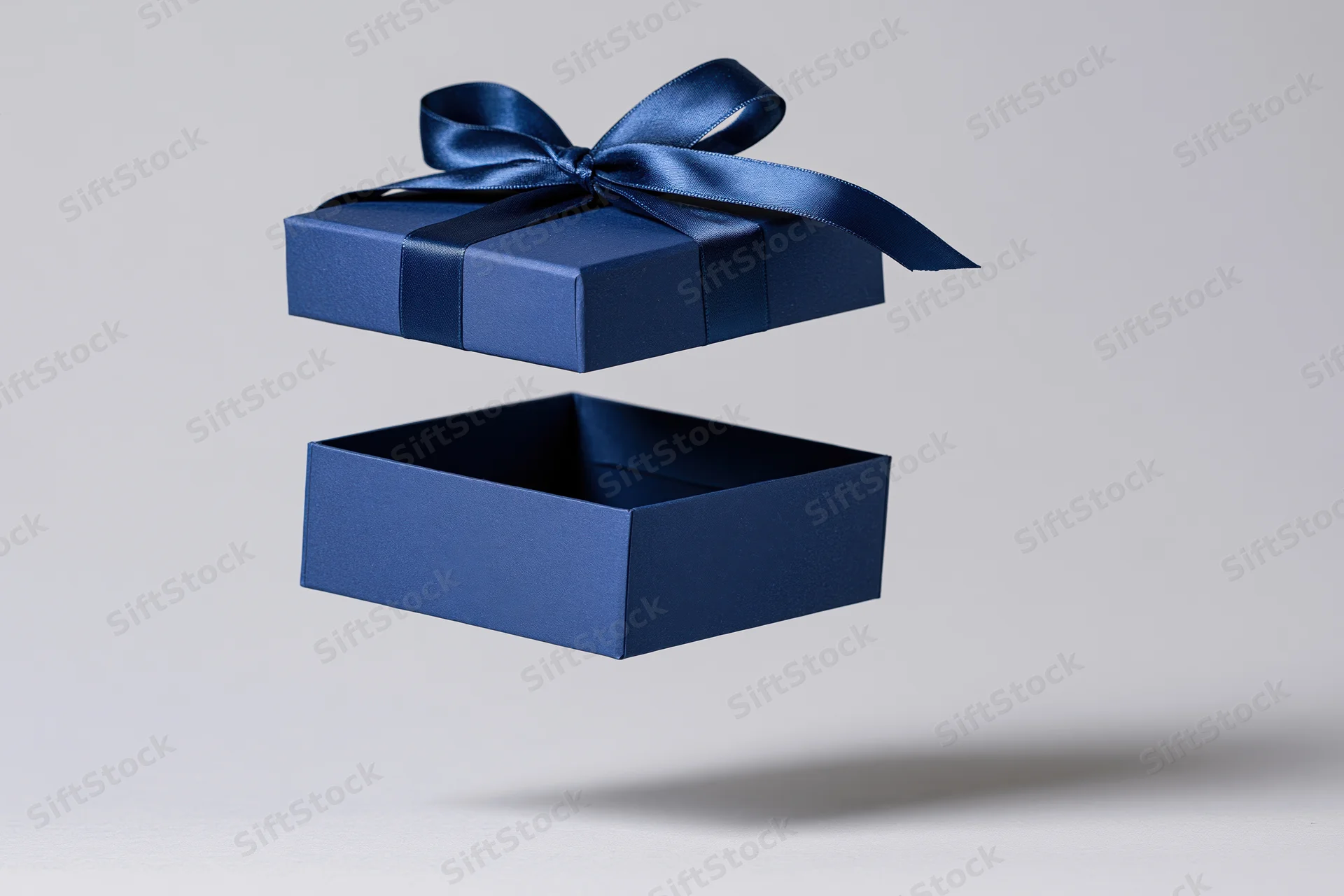 Floating blue gift box lid with satin ribbon above open base against white background