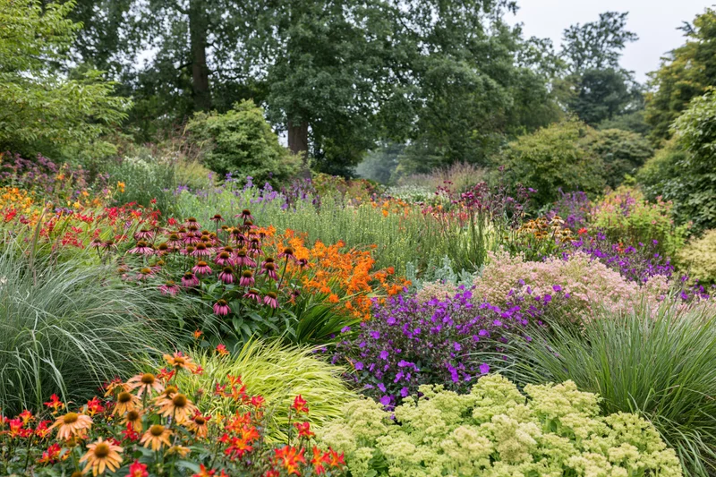 Densely planted perennial garden border in full bloom with colorful flowers and green foliage under overcast sky