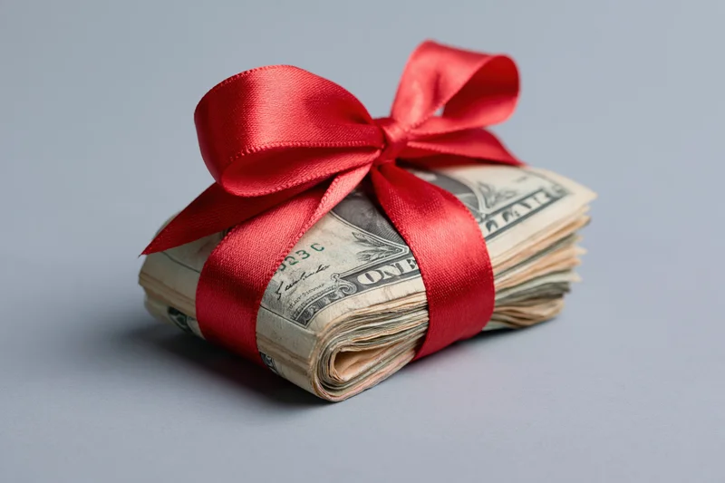 Stack of us dollar bills wrapped with red satin ribbon on gray surface